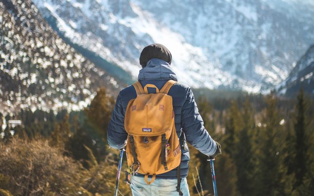 Person hiking with a yellow backpack infront of snow covered hills